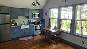 A kitchen with grey cabinets, a stainless steel refrigerator, a microwave, and a stove. There is a dining table with chairs and a window with curtains. -  Loft apartment in a working horse barn.  Minutes from Lexington and the  VAHC. (Lexington)