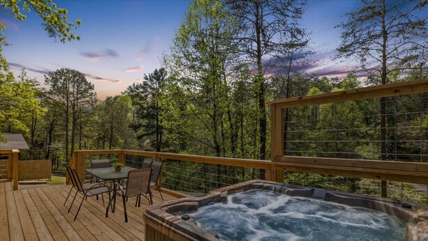 Una terraza de madera con un jacuzzi, asientos exteriores y una vista panorámica de árboles y montañas.