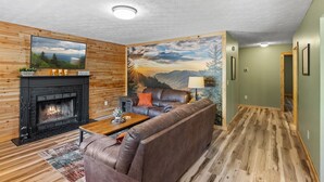 Una sala de estar acogedora con chimenea, un sofá de cuero y un gran mural de un paisaje montañoso.