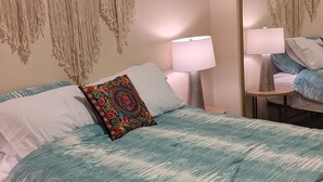 Una camera da letto con un letto, due lampade da comodino, un arazzo macramè e uno specchio.