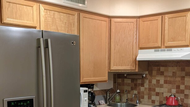 Una cucina funzionale con mobili in legno, frigorifero in acciaio inossidabile, forno a microonde e fornello a gas.