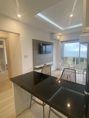 A modern kitchen with a black countertop, white chairs, a built-in TV, and a balcony with a view. - 25homeapart (Encarnacion)