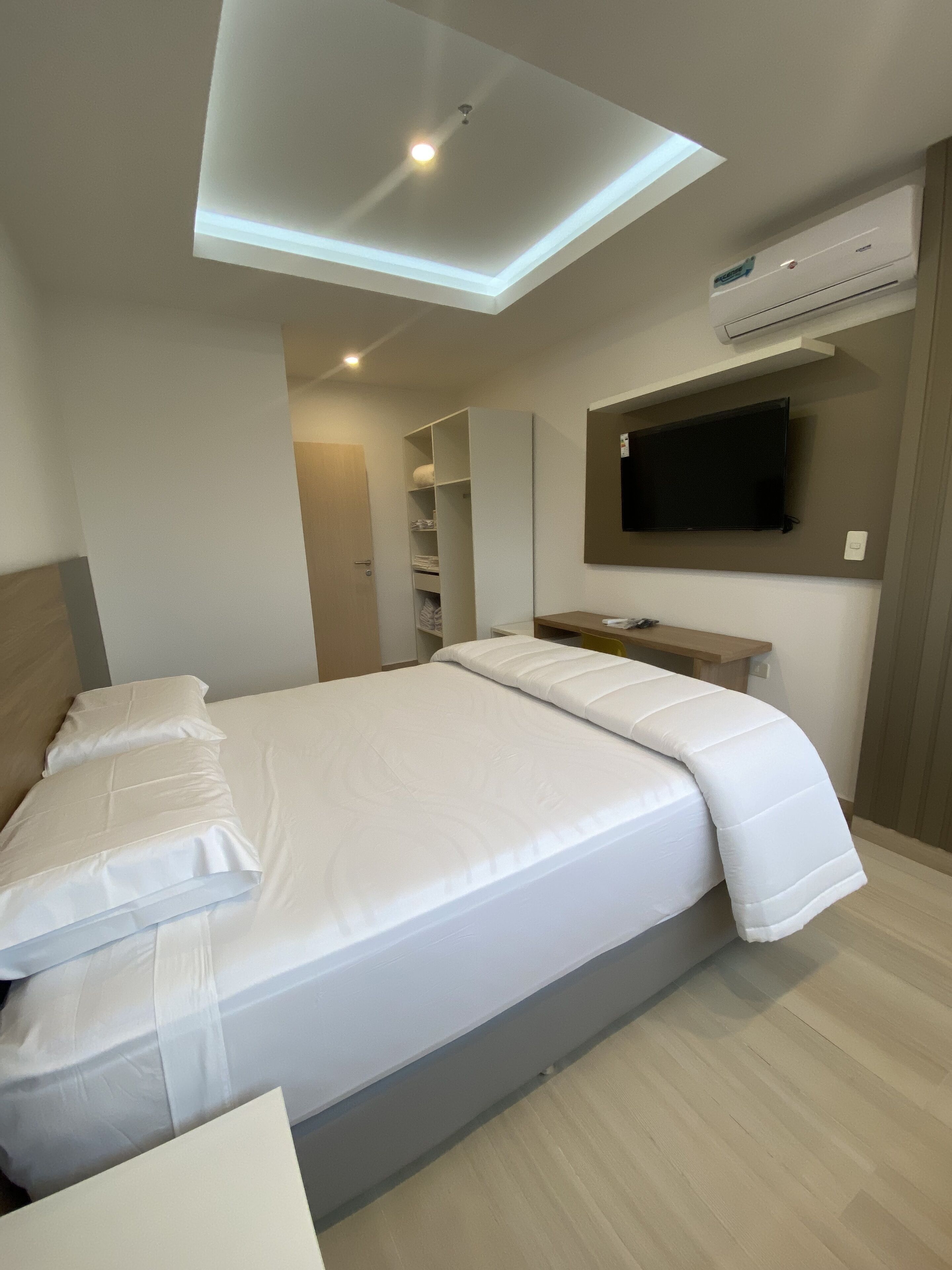 Ein modernes Hotelzimmer mit einem großen Bett, integrierten Regalen, einem Flachbildfernseher und einer Klimaanlage.
