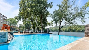 Ein Schwimmbecken mit Blick auf einen See und Bäume, umgeben von einem Gebäude mit einer Ziegelmauer und Liegestühlen.
