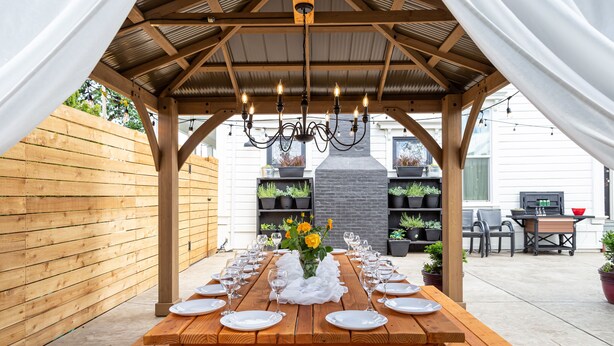 An outdoor wooden pergola with a dining table set for six, surrounded by potted plants and a brick fireplace. - Room for Everyone! 7BR, 6.5BA Wine Country Retreat near Downtown (McMinnville)