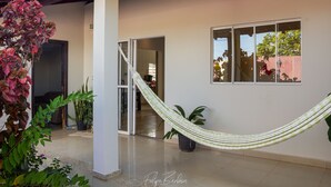 A covered outdoor area with a hammock, potted plants, and a doorway leading to an interior space. - Hostel Santa Rita (Santa Rita De Cassia)