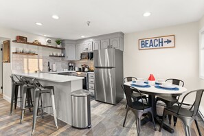Una cucina moderna con isola centrale, sgabelli da bar, tavolo da pranzo con sedie e un cartello con la scritta 'BEACH'.