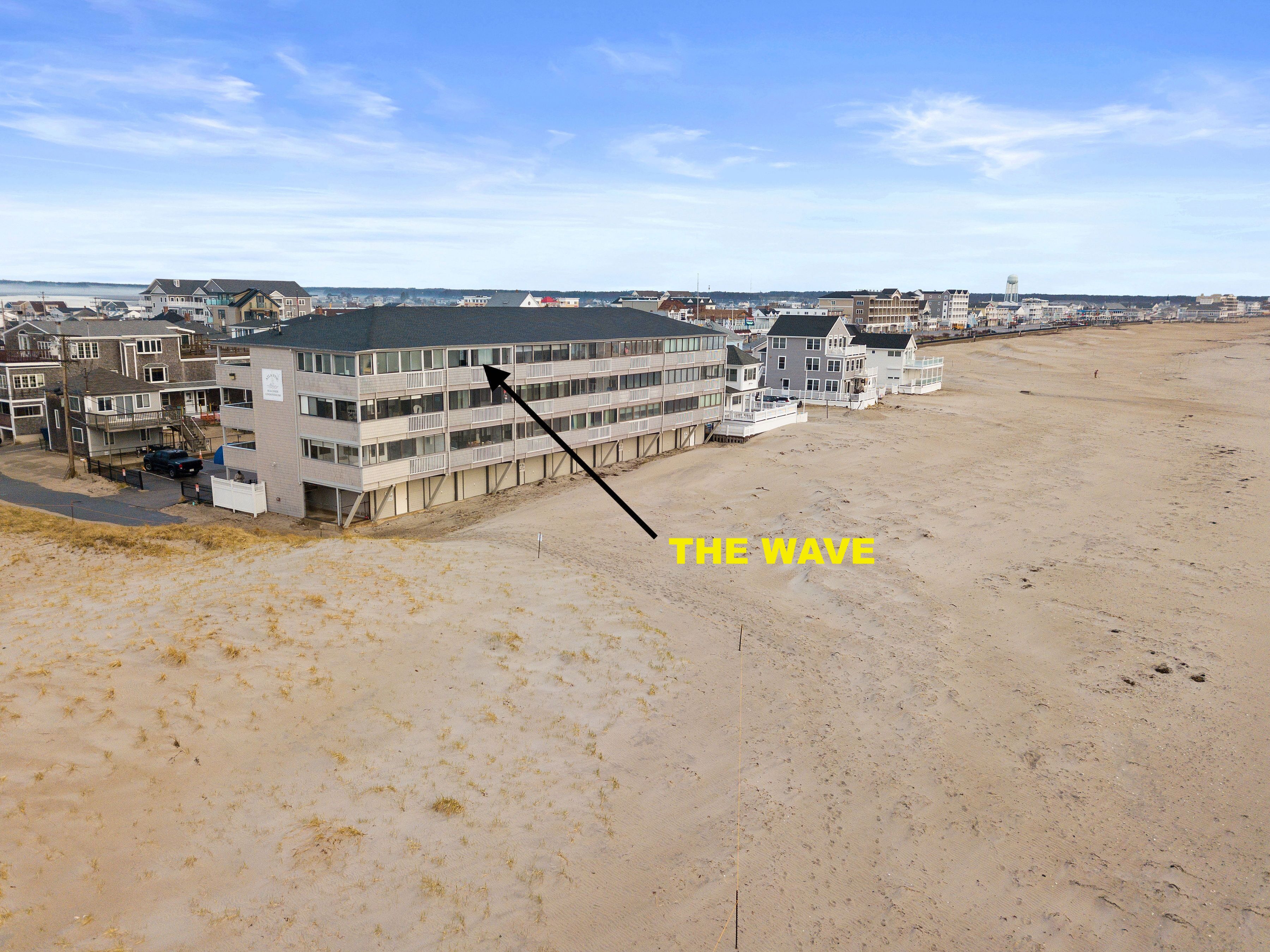 A beachfront hotel with multiple floors, a sandy beach in front, and a clear sky.