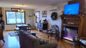 A spacious living room with a large gray sofa, wooden flooring, a fireplace, and a television.