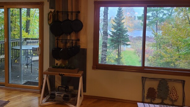 A room with a large window overlooking a forested area, a wall-mounted pot rack, and a sign reading "every end BEGINNING".