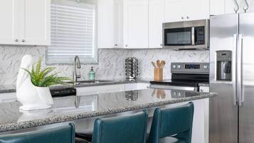 Cocina moderna con armarios blancos, encimera de granito, refrigerador de acero inoxidable y taburetes de bar color turquesa.