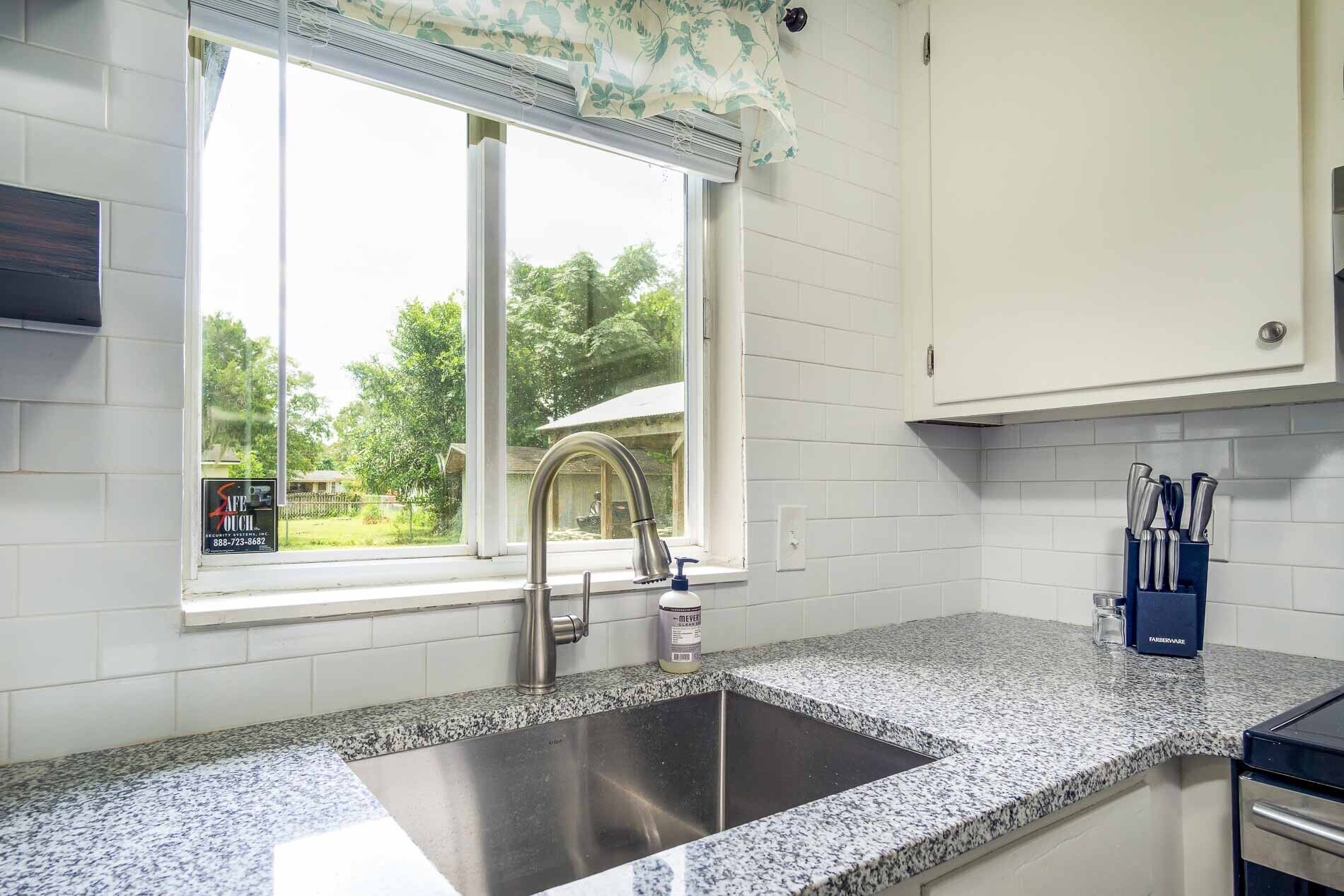 A kitchen with a granite countertop, stainless steel sink, and a window with a view of greenery outside.