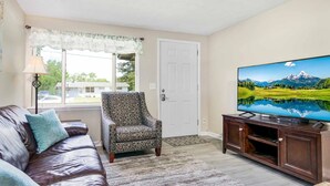 Ein Wohnzimmer mit Ledersofa, Ohrensessel und Fernseher auf einem Holzboden.