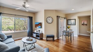 A spacious living room with a ceiling fan, a large wall clock, a dining area with a table and chairs, and a sofa. - Enjoy Paradise in this Quiet, Resort-Style 2 BR Condo (Fountain Hills)