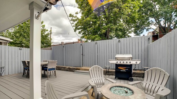 Un patio extérieur couvert, équipé d’un barbecue, de sièges et d’un foyer.