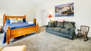 Une chambre à coucher avec un lit en bois, un canapé gris, un fauteuil à bascule et un tableau représentant un paysage urbain accroché au mur.