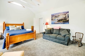 Un dormitorio con una cama de madera, un sofá gris, un sillón mecedor y un cuadro de un paisaje urbano en la pared.