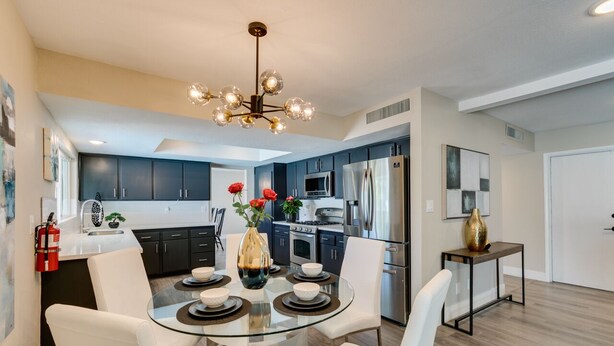 A modern kitchen with dark cabinets, stainless steel appliances, and a glass dining table with white chairs.