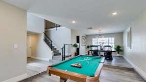 A pool table in a spacious room with a staircase leading to another area.
