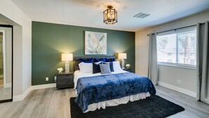 A bedroom with a bed, nightstands, a lamp, a painting, and a window with curtains.