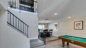 A spacious room with a pool table, a dining area, and a staircase leading to an upper level.