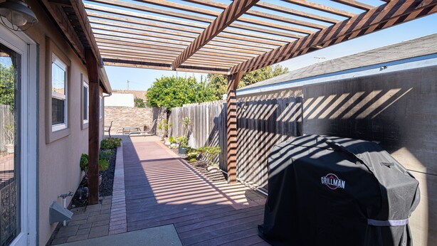 Un espacio de patio cubierto con una parrilla, un pérgola de madera y un camino de ladrillo.