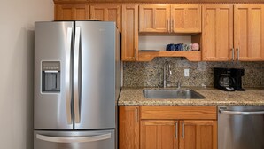 Una cocina con armarios de madera, un refrigerador de acero inoxidable, una encimera de granito, un lavamanos y un lavavajillas.