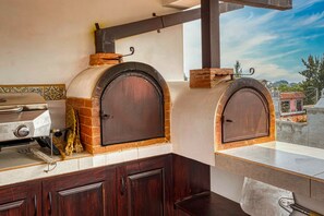 Una cocina con dos hornos de leña, una parrilla y vistas a la ciudad.