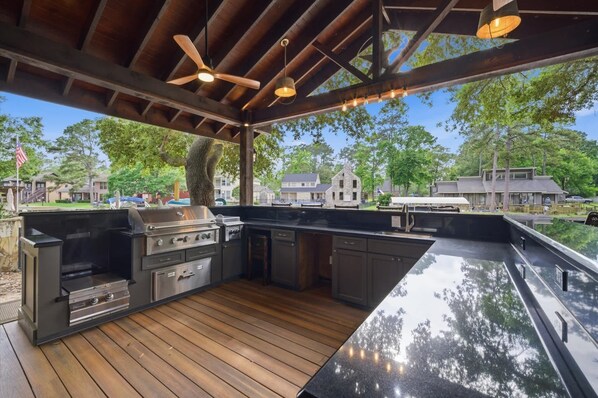 An outdoor kitchen with a grill, built-in cabinets, and a wooden deck.