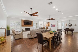 A spacious living room with a fireplace, ceiling fans, a dining area with a wooden table and chairs, and a billiards table.
