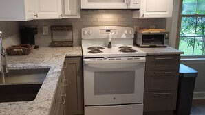 Una cocina moderna con armarios blancos, microondas integrado, estufa y tostadora.