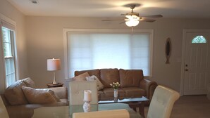Una sala de estar con una mesa de comedor de cristal, dos sofás, un ventilador de techo y una puerta con un vitral.