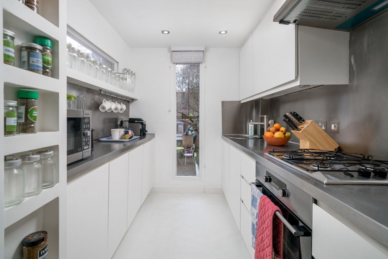 A narrow kitchen with white cabinets, a stainless steel stove, and various kitchen utensils.