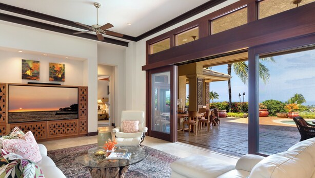 A spacious living room with a large flat-screen TV, comfortable seating, and a view of the outdoor patio area.
