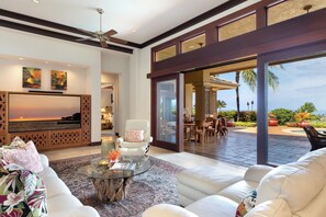 A spacious living room with a large flat-screen TV, comfortable seating, and a view of the outdoor patio area. - Mauna Kea Moani Heights #16 Custom Home - Stunning Sunsets Pool/Spa- Club Member (Kamuela)