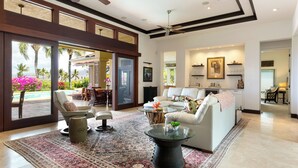 A spacious living room with a large window, a ceiling fan, and a view of a pool and palm trees.