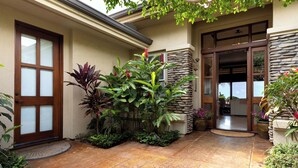 A house with a stone exterior, a wooden door with frosted glass panels, and a tiled patio area with various plants.