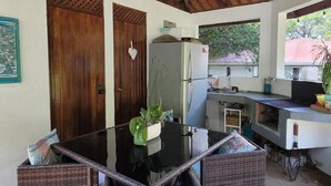 Una cocina compacta con refrigerador, pileta y pequeño comedor con mesa de vidrio y sillas de mimbre.