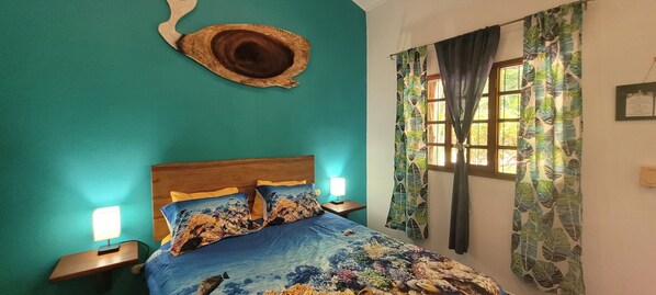 A bedroom with teal walls, a wooden headboard, a bed with a floral bedspread, two bedside lamps, and a window with curtains.