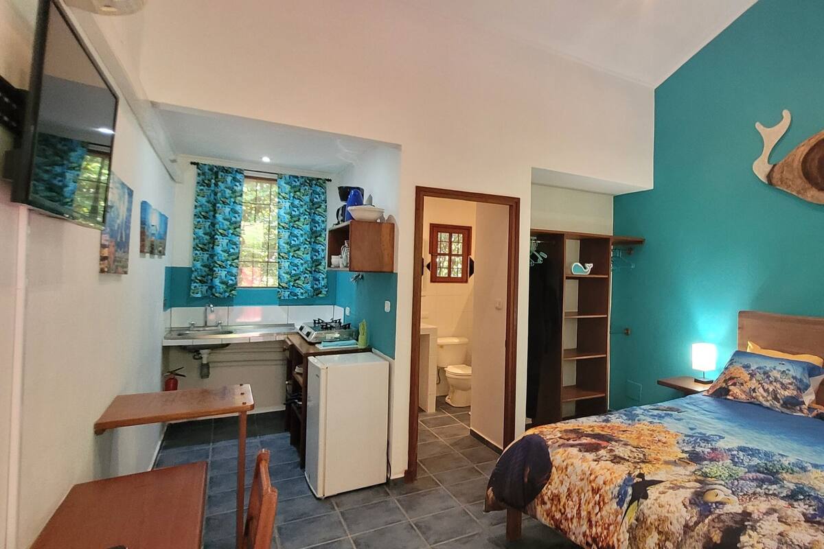 A compact bedroom with a bed, bedside tables, a small desk, and a window with curtains.