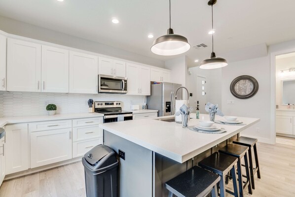 A modern kitchen with white cabinets, stainless steel appliances, and a large island with bar stools. - In the Heart of Tempe (Tempe)