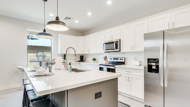 Una cocina moderna con armarios blancos, electrodomésticos de acero inoxidable y una isla central con taburetes.