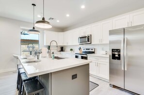 A modern kitchen with white cabinets, stainless steel appliances, and a central island with bar stools. - In the Heart of Tempe (Tempe)