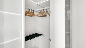 A modern, minimalist walk-in closet with white walls, a metal rod rack for hanging clothes, and a black shelf unit.
