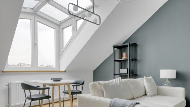 A modern loft apartment with a skylight, a dining area, a gray sofa, and a bookshelf.