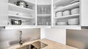 A kitchen with a built-in oven, a sink, and open cabinets containing dishes and cookware.