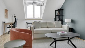 A modern living room with a sofa, a pink armchair, a coffee table, a desk, and a bookshelf.