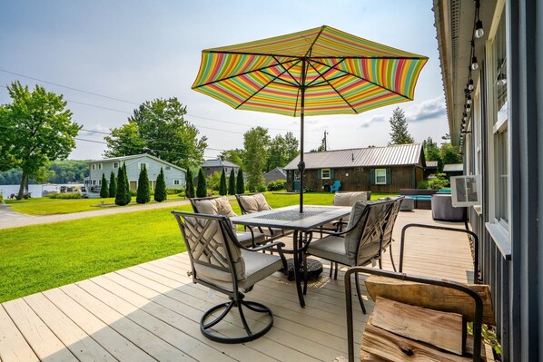 A deck with a table and chairs, an umbrella, and a view of a lake and houses.