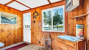 A wooden cabin interior with a large window, a door, a wooden desk, and a rack of fishing rods.