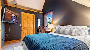 A bedroom with a bed, a television mounted on the wall, a wooden door, and a window.